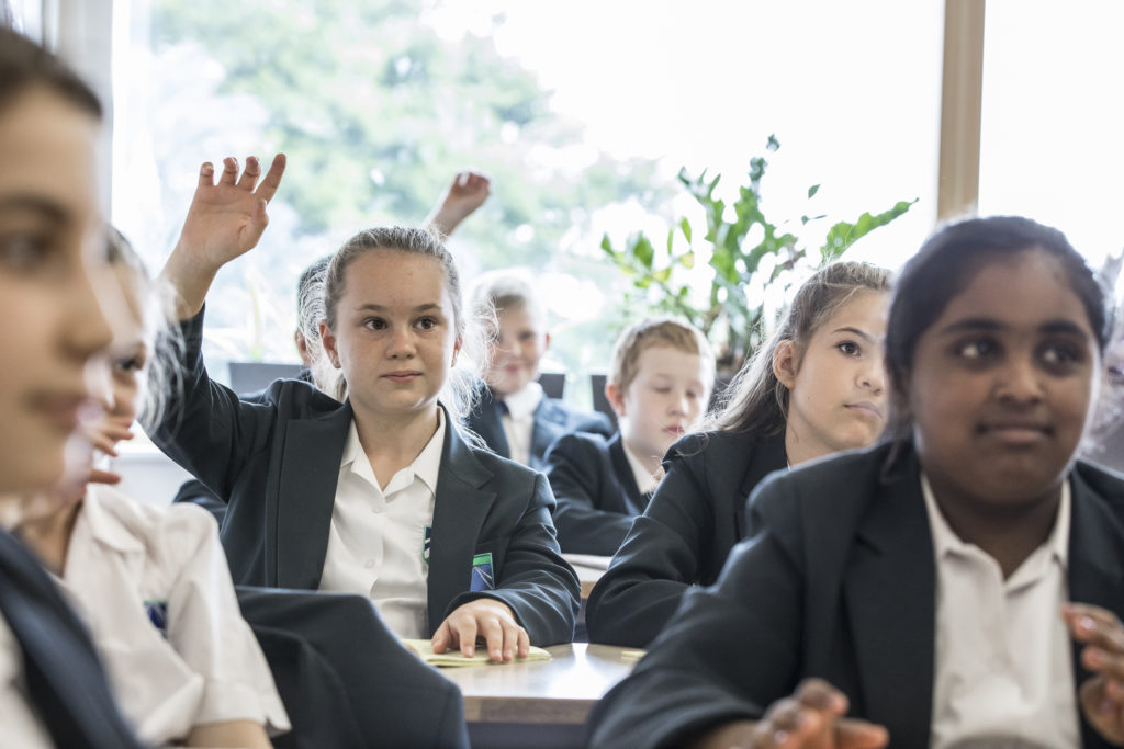 Class of Leigh Academy students looking to the front of the room, some with their hands up to ask questions.