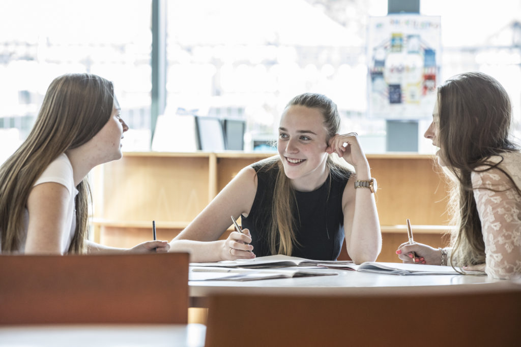 Three female Leigh Academy students sitting at a table, working together.