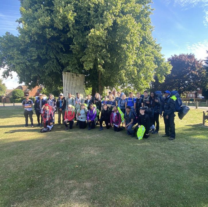 A large group of students are seen posing for a photo together outdoors, wearing backpacks and outdoor clothing.