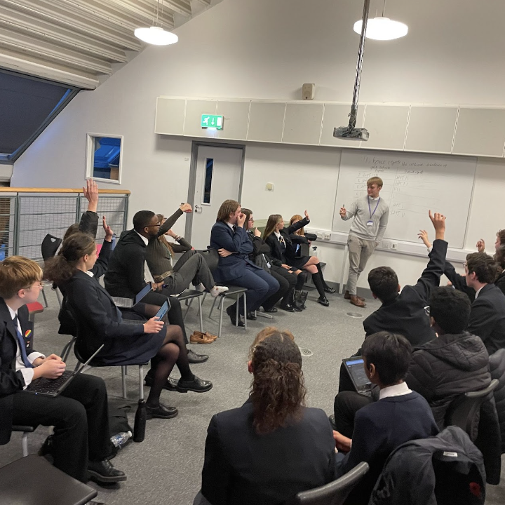 Photo showing a class of students interacting with a male member of staff conducting a lesson in a classroom.