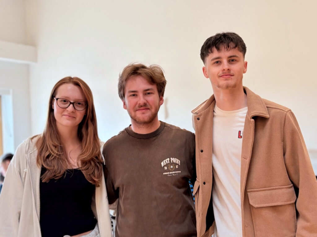 Three young people are standing together, posing for the camera