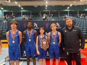 Four gymnasts with medals and a trophy picture with there coach inside an arena